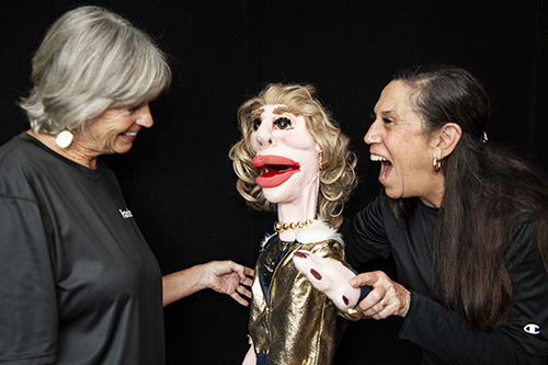 Joan with a puppet laughing with a helper smiling